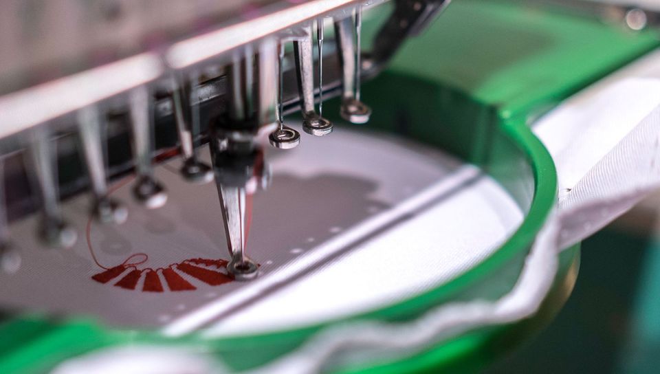 Máquina bordadora trabajando un diseño en hilo rojo sobre tela blanca.